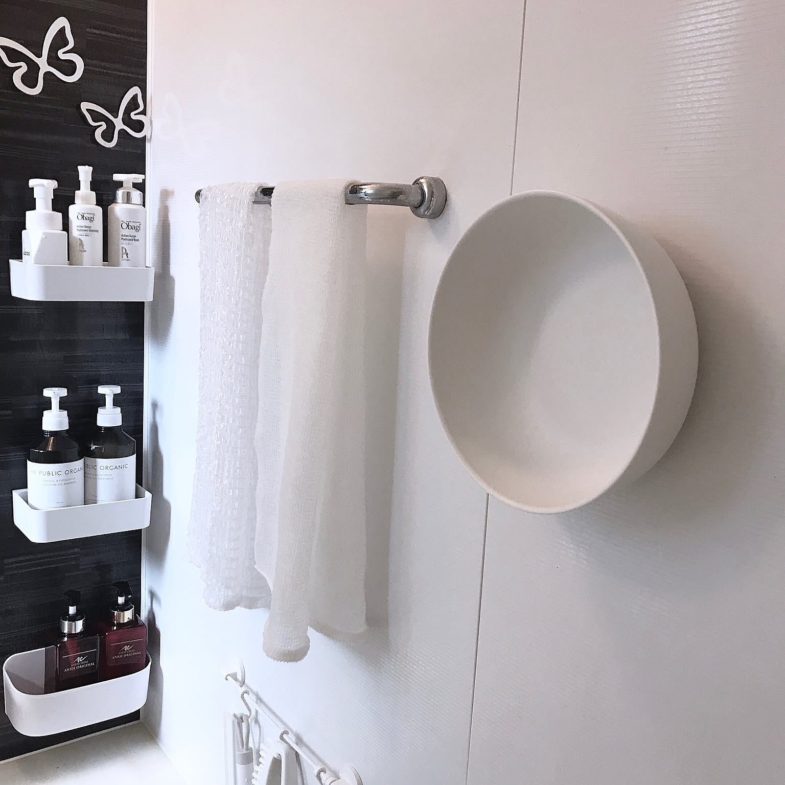 A magnetic wash basin mounted on a bathroom wall beside white wall shelves and hanging cleaning tools.
