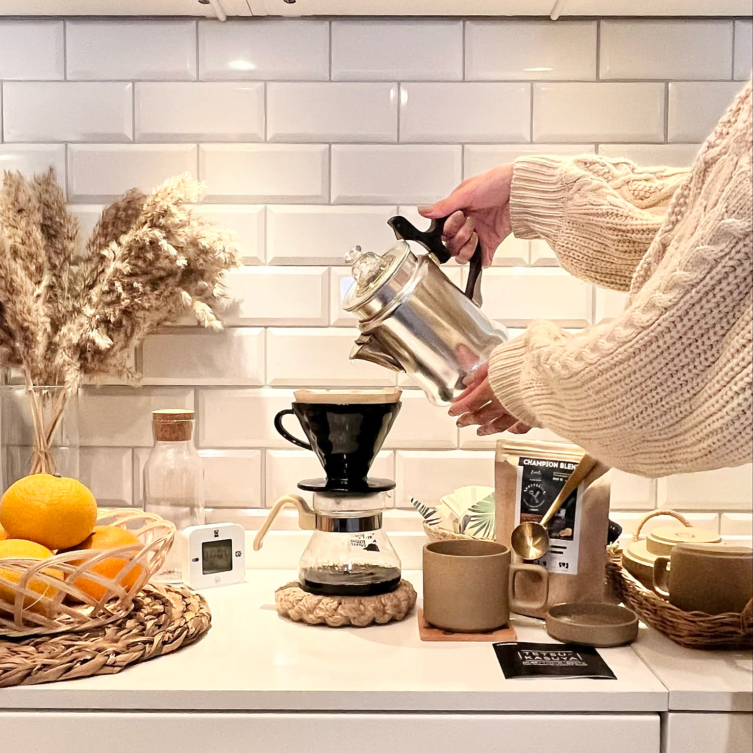 A black HARIO V60 02 dripper brewing coffee into a glass server on a bright kitchen counter.