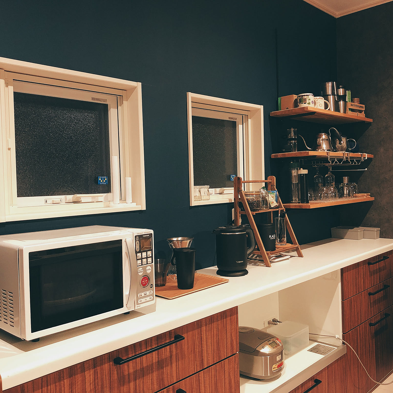 A compact Zojirushi 3-cup rice cooker stored on a lower shelf in a narrow kitchen.