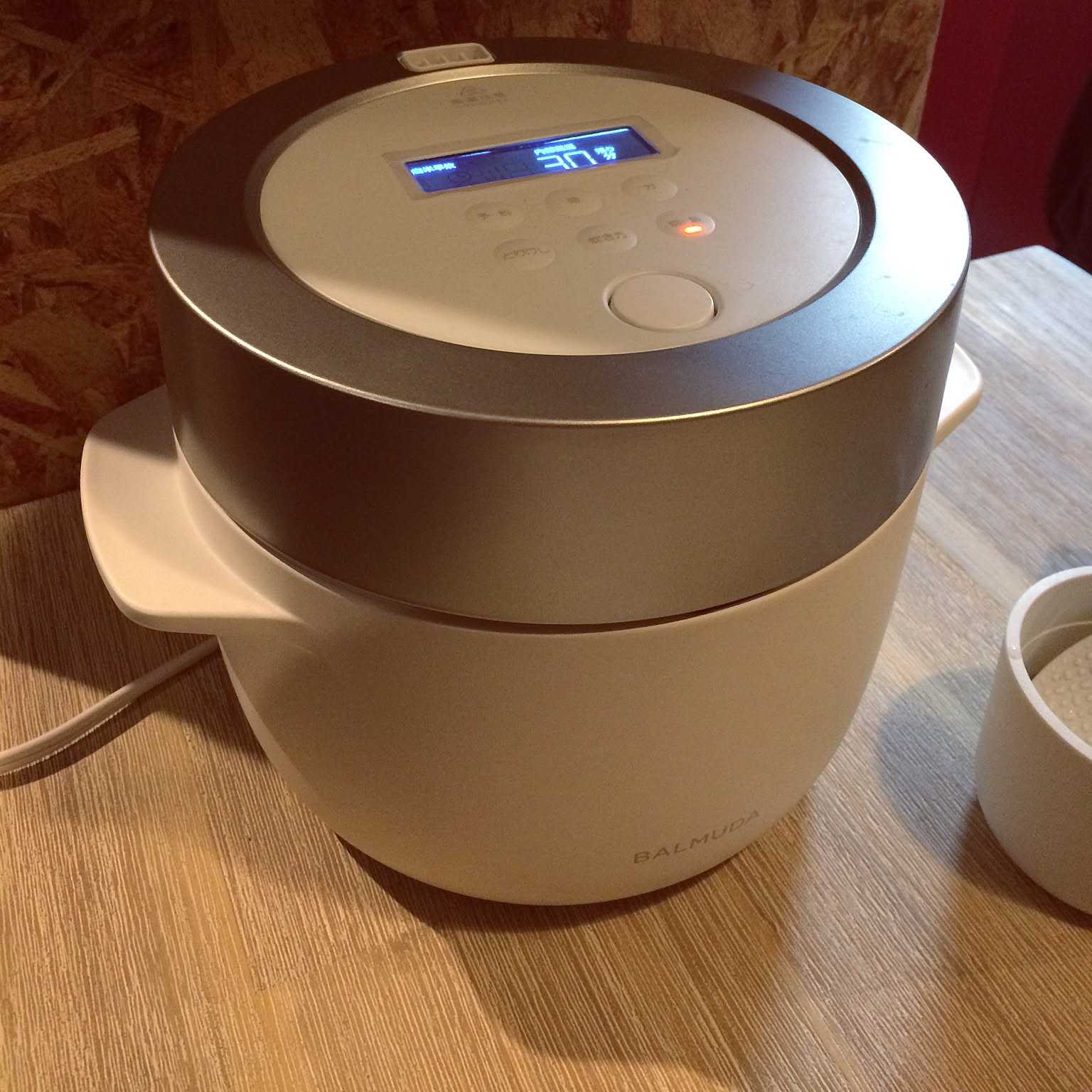 A BALMUDA The Gohan rice cooker showing its two-part steam-cooking design, a metal lid ring over a white body, with the BALMUDA wordmark