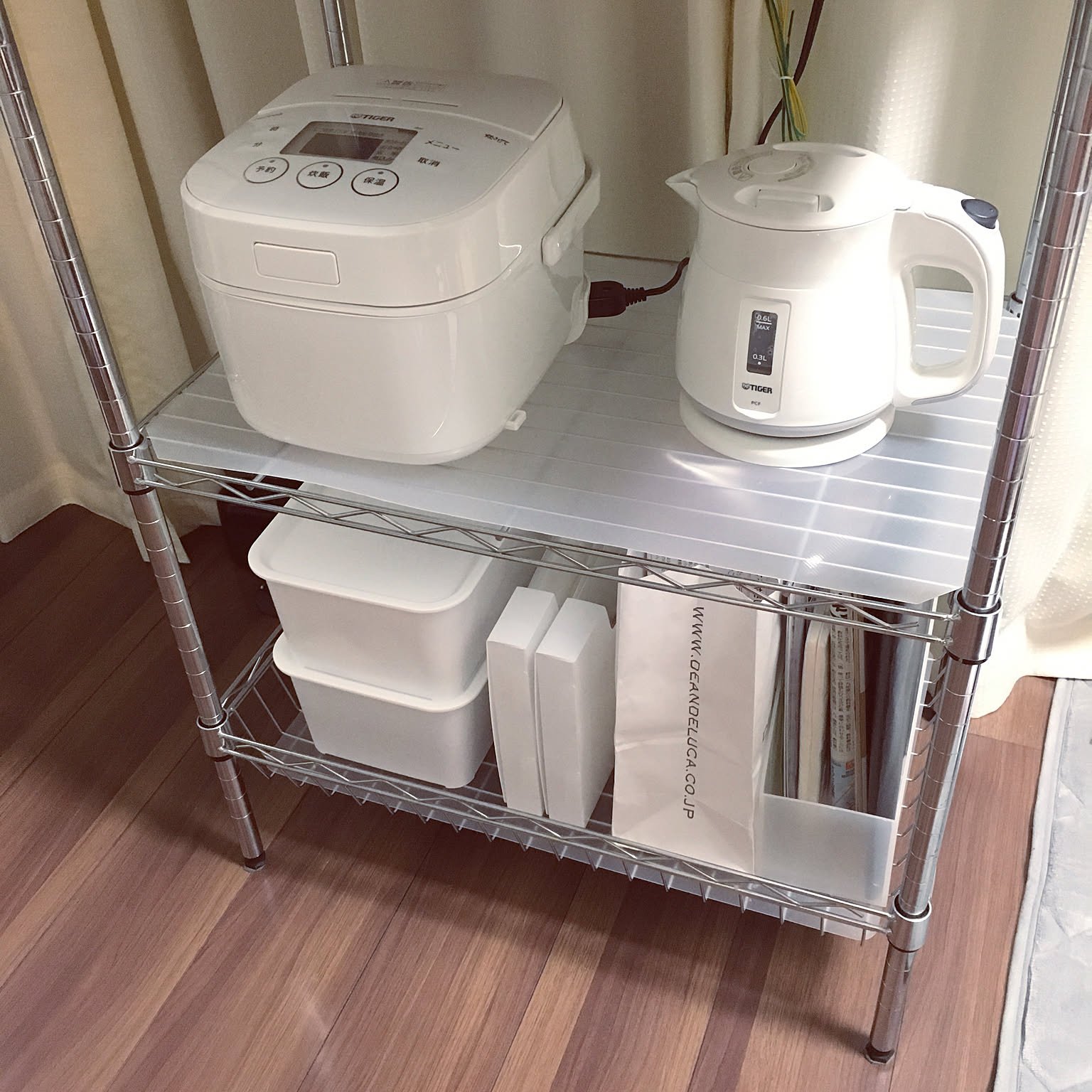 A white Tiger compact rice cooker stored on a metal rack beside a small kettle.