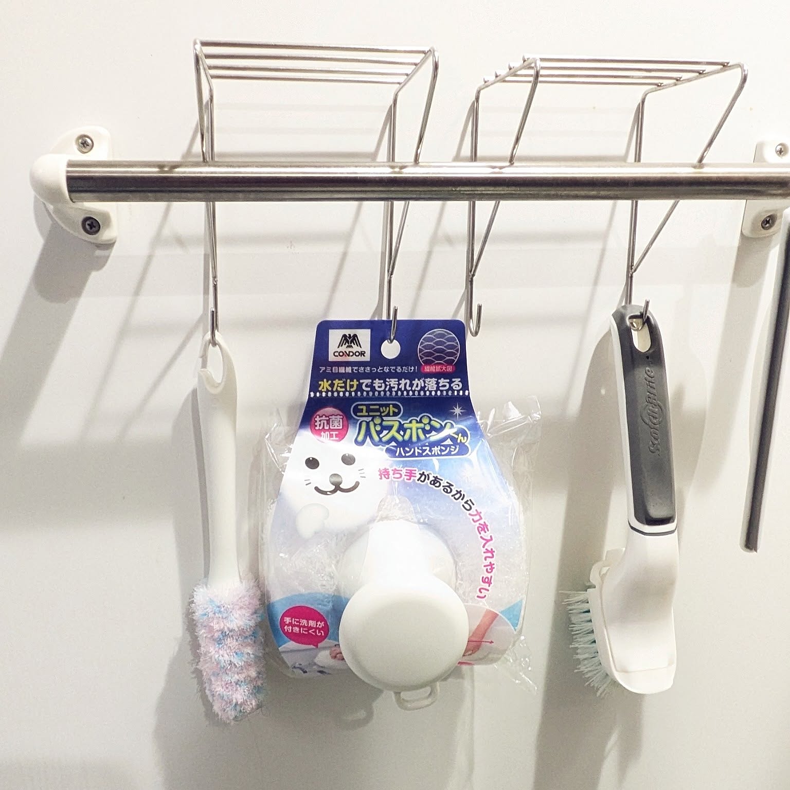 Bathroom cleaning brushes, a sponge, and a squeegee hanging separately from a towel bar.