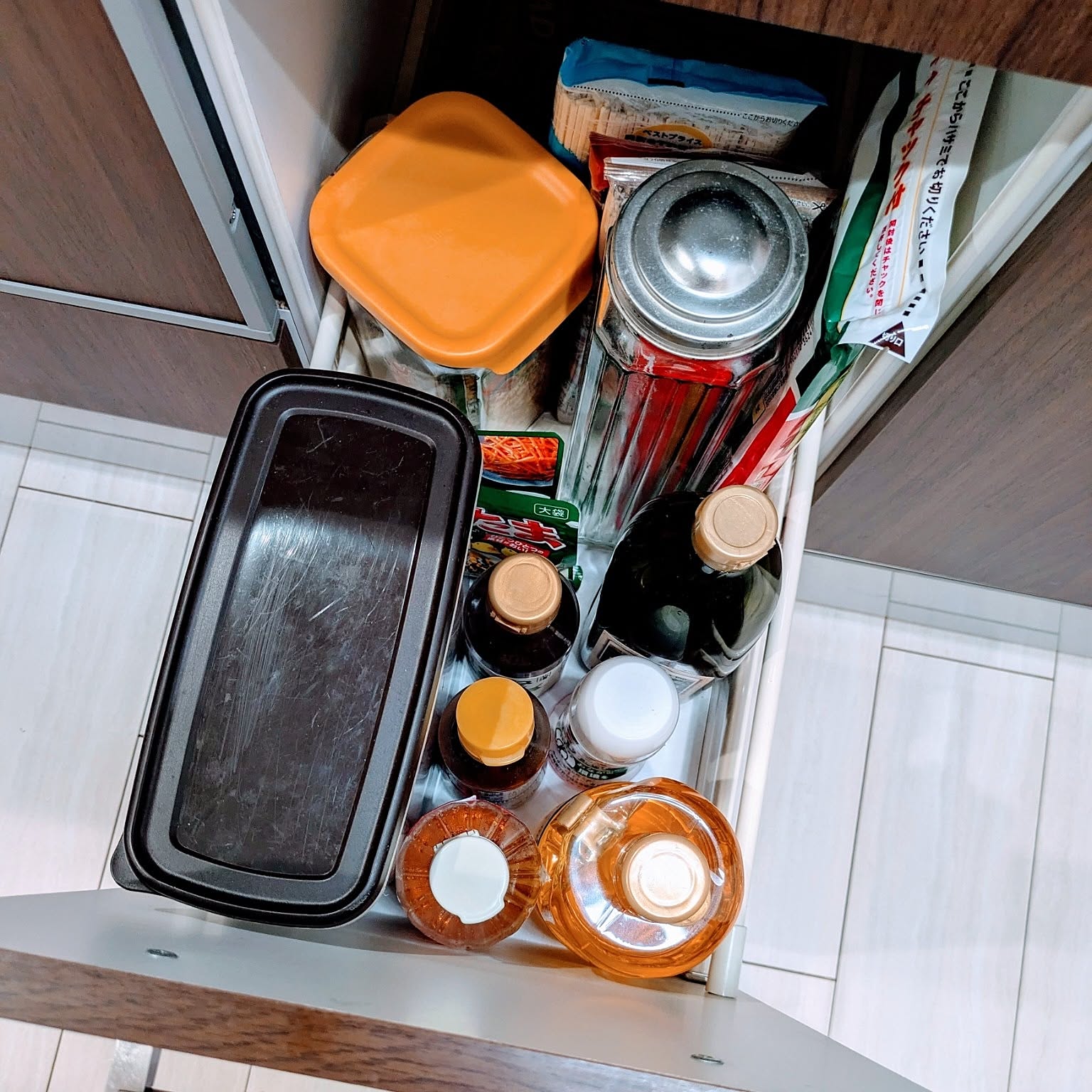A narrow kitchen drawer storing bottles, pasta, dry noodles, seasonings, and food packets upright.